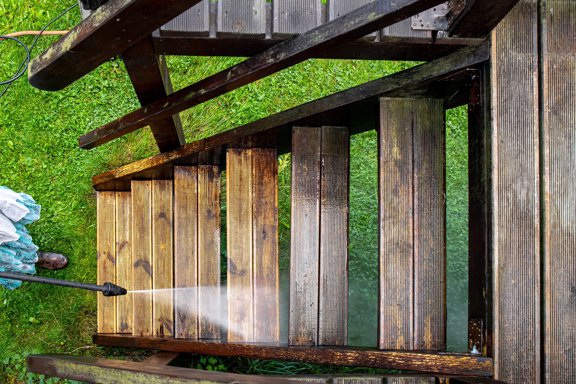 Close up view of using pressure washer to clean impregnated wood terrace stairs outdoors in the spring. Before cleaning and after, big contrast in color.