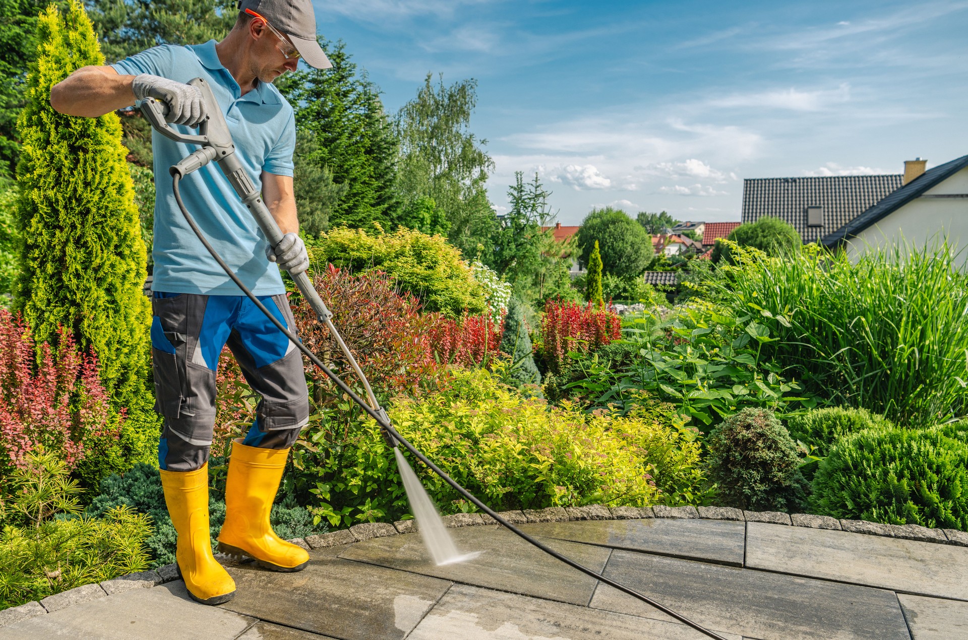 Man Using Pressure Washer to Clean Patio in Lush Garden During Sunny Day